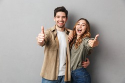 Happy young couple showing thumbs up and looking at camera isolated over gray background