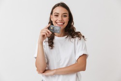 Portrait of a smiling young casual brunette woman holding credit card isolated over white background
