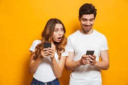 Image of young woman spying and peeking at smartphone of her boyfriend isolated over yellow background