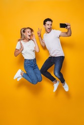 Photo of happy excited young loving couple jumping isolated over yellow wall background make a selfie.