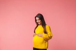 Image of a beautiful young pregnant emotional woman posing isolated over pink background.