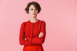 Portrait of an upset beautiful young woman wearing red clothes standing isolated over pink background