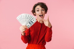 Portrait of a beautiful young woman wearing red clothes standing isolated over pink background, showing money banknotes