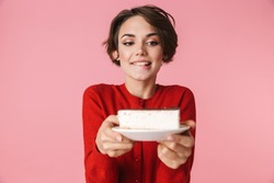 Portrait of a beautiful young woman wearing red clothes standing isolated over pink background, holding piece of cake on a plate