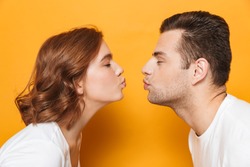 Close up of a beautiful couple wearing white t-shirts standing isolated over yellow background, kissing