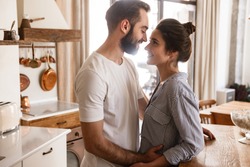 Image of adorable brunette couple in love man and woman 20s smiling while hugging together in apartment