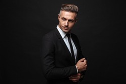 Portrait of european unshaven businessman dressed in formal suit posing and looking aside isolated over black wall