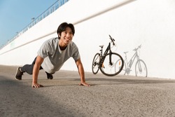 Young fit man bicyclist working out oudoors, doing push-ups