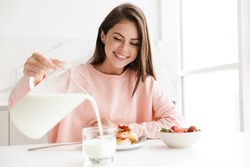 Beautiful smiling young girl having tasty healthy breakfast while sitting at the kitchen table