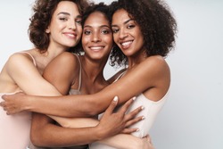 Portrait of three adorable multiethnic women smiling and hugging together isolated over white background