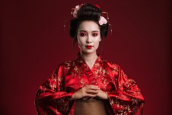 Image of beautiful young geisha woman in traditional japanese kimono isolated over red background