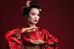 Image of young asian geisha woman in traditional japanese kimono dancing isolated over red background