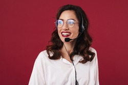 Picture of positive smiling young woman work in callcenter isolated over red wall background talking by cellphone.