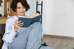 Smiling young woman entrepreneur reading book while sitting in the office