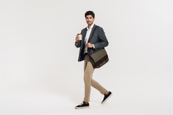 Photo of pleased caucasian businessman drinking coffee while walking with bag isolated over white wall