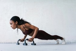 Photo of young african american sportswoman working out with push-up stops indoors