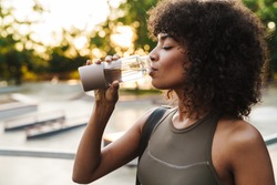 Image of african american sportswoman drinking water while working out on sports ground