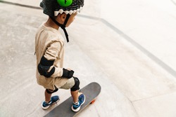 Young boy wearing safety gear at the skateboard park, back view