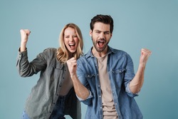 Young excited man and woman screaming and making winner gesture isolated over blue background