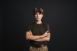 Confident beautiful soldier woman standing isolated over black background, arms folded