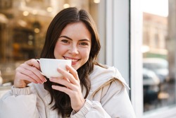 Cheerful young woman having tea with cake at the cafe outdoors