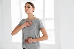 Athletic young sportswoman doing breathing exercise during yoga practice indoors