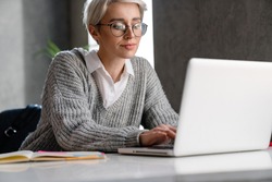 White-haired focused woman working with laptop while sitting at table in office