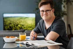 Young man with down syndrome smiling and doing home work in kitchen at home