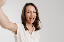 Young european woman winking while taking selfie photo isolated over white background