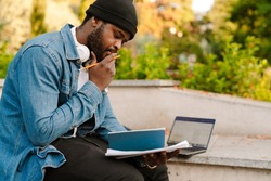 Black man working with laptop and papers while sitting on bench in park