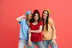 Three young happy girls smiling and posing at camera isolated over red background