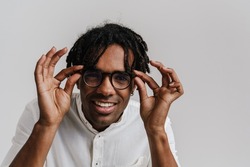 Joyful african man adjusting glasses and looking at camera isolated over white background