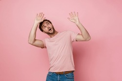 Emotional young bearded man in pink t-shirt looking upward and gesturing while posing over isolated pink studio wall