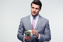 Handsome businessman counting US dollars over gray background and looking at camera
