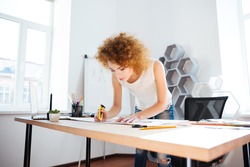Serious attractive young woman photographer with curly red hair working in office using stationery knife