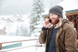 Happy bearded young man talking on mobile phone outdoors in winter