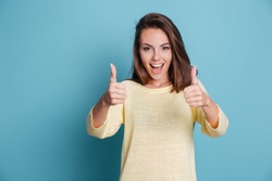 Smiling pretty young woman showing thumbs up isolated on the blue background