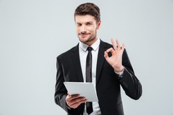 Happy young businessman with tablet winking and showing ok sign over white background