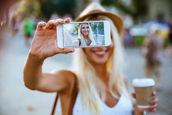 Young smiling cheerful blonde girl making selfie while standing on the street