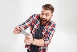 Excited bearded man in plaid shirt playing on smartphone over white background