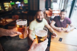 Closeup of waiter bringing two glasses of beer for two smiling bearded men sitting in pub