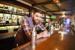 Portrait of cheerful young bartender standing and smiling in bar 
