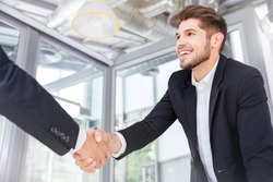 Two smiling successful young businessmen shaking hands on business meeting in office