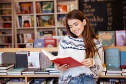Portrait of a pretty smiling girl reading book indoors in library