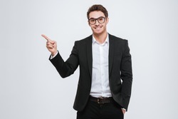 Portrait of a happy businessman in eyeglasses pointing finger away over white background
