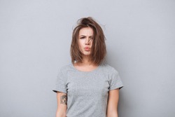 Portrait of a young upset girl in t-shirt looking at camera isolated on a gray background