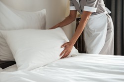 Cropped image of a female chambermaid making bed in hotel room