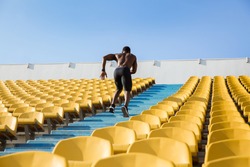 Back view of a young male athlete exercising by running upstairs at the stadium