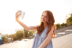 Happy redhead girl with long hair taking a selfie while standing over city street background