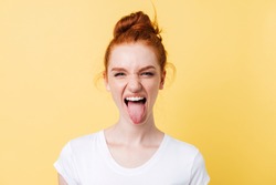 Funny ginger woman showing tongue and looking at the camera over yellow background